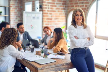 Group of business workers working together. Middle age beautiful businesswoman standing smiling happy looking at the camera at the office